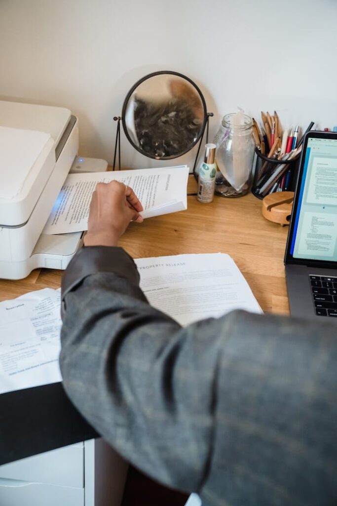 Focused professional working on documents with laptop and printer nearby.
